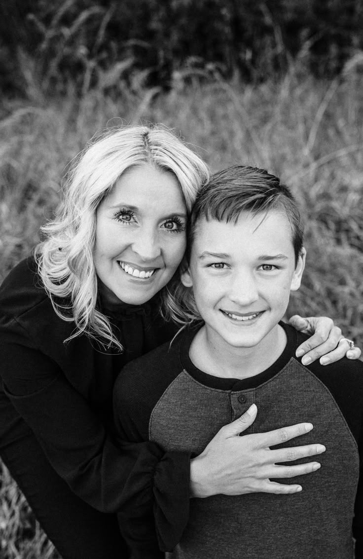 a mother and son posing for a black and white photo in the grass with their arms around each other