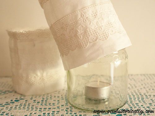 a candle in a jar on a table next to two pillows and a lace doily