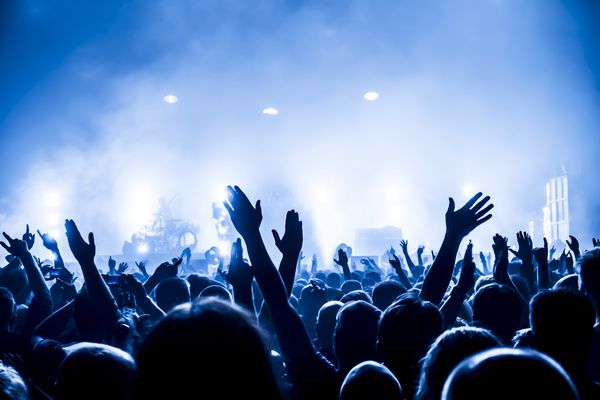 a crowd of people at a concert with their hands in the air and lights on