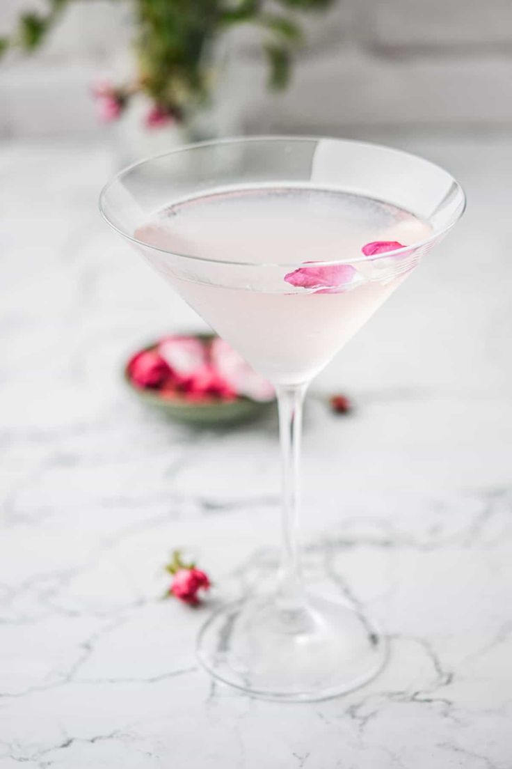 a martini glass filled with white wine and garnished with pink flowers on the rim