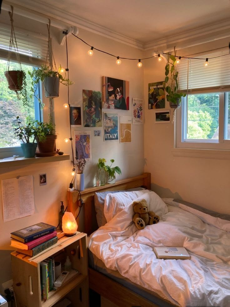 an unmade bed in a small room with lights strung from the ceiling above it