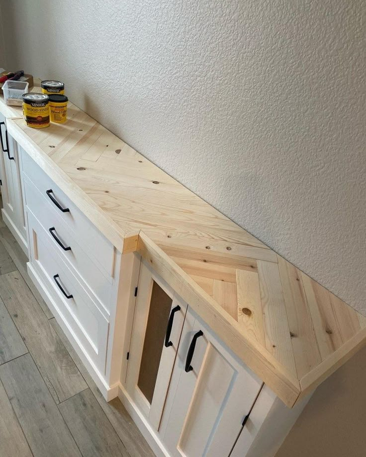 a kitchen counter made out of wood and white cupboards with drawers on each side