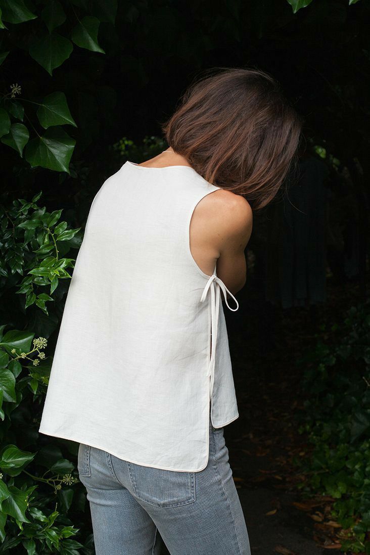 a woman in jeans and a white top is looking down at the ground with her back to the camera