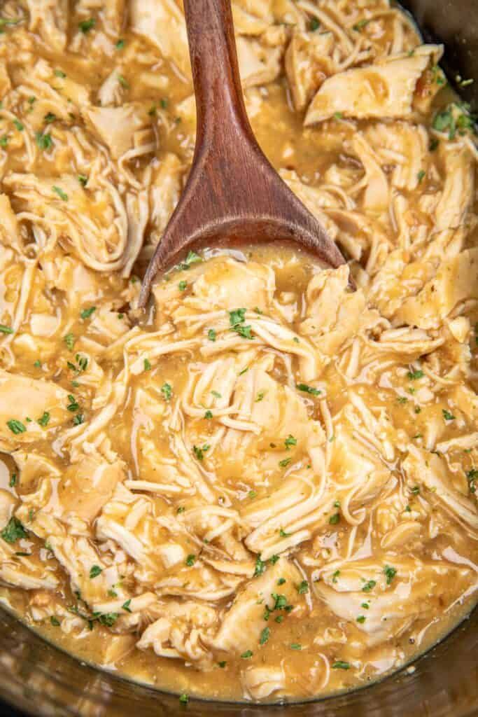 a wooden spoon in a slow cooker filled with chicken and noodles