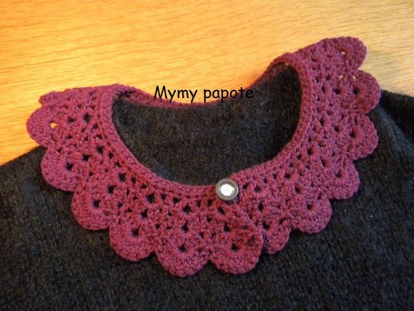 a pink crocheted collar on top of a black sweater next to a wooden table