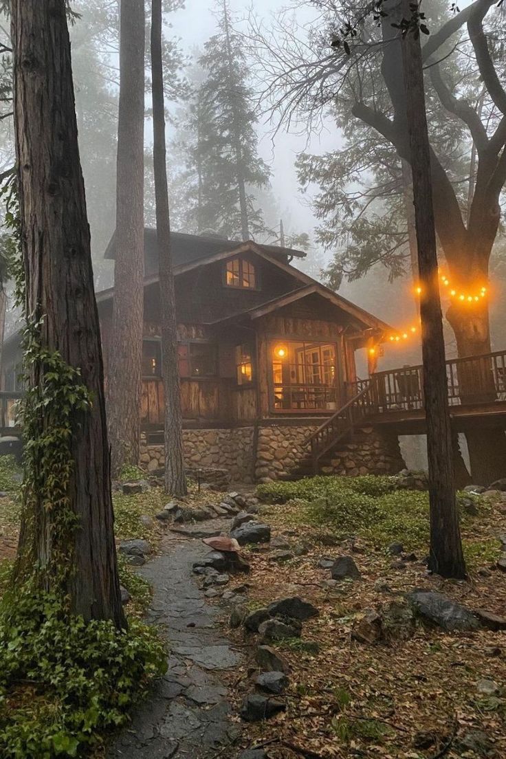 a cabin in the woods with lights on it's porch and stairs leading up to it