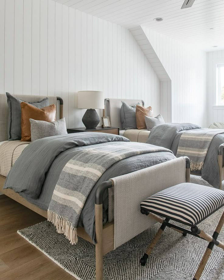 two beds in a bedroom with white walls and wood flooring, one has a striped blanket on the bed