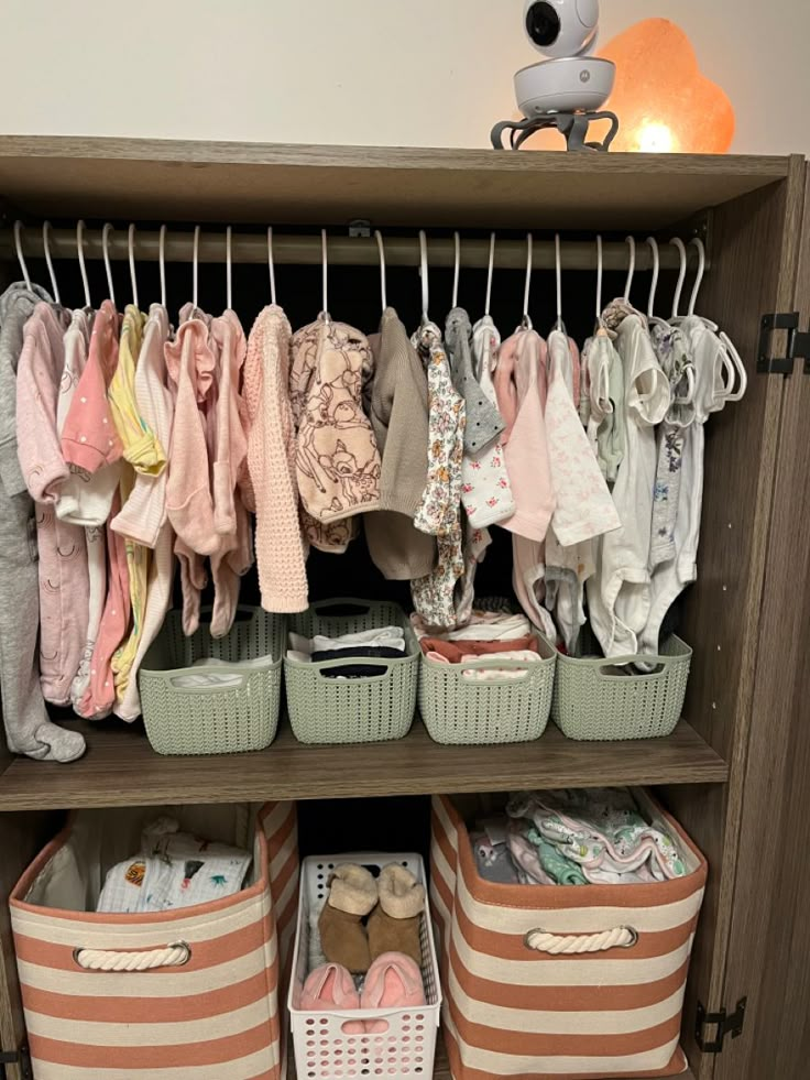 a closet filled with lots of baby clothes next to a stuffed animal on top of a wooden shelf