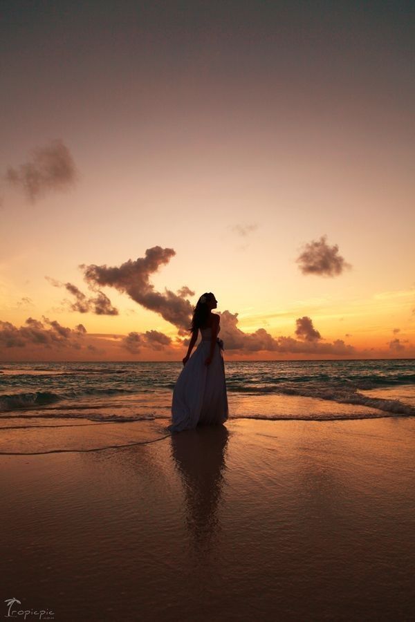 a woman standing on top of a sandy beach next to the ocean at sunset or dawn