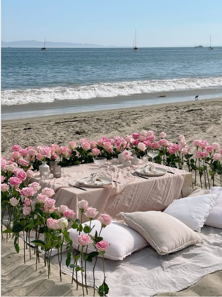 a table set up on the beach with pink flowers