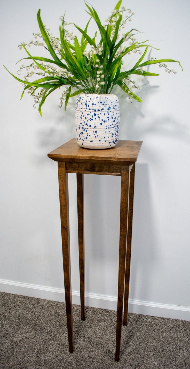 a small wooden table with a plant on top and a white vase sitting on it