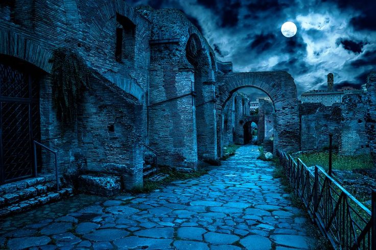 a dark alley with cobblestones leading into an old building under a full moon