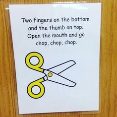 a pair of yellow scissors sitting on top of a piece of paper next to a sign that says two fingers on the bottom and the thumb on top