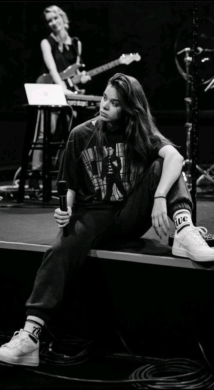 a man sitting on top of a stage next to a woman with long hair holding a microphone