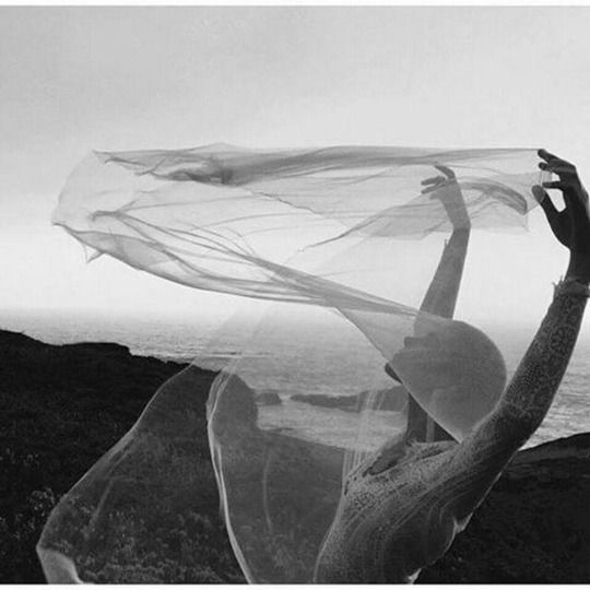 a woman is standing on top of a hill with her arms in the air while holding a sheer fabric over her head