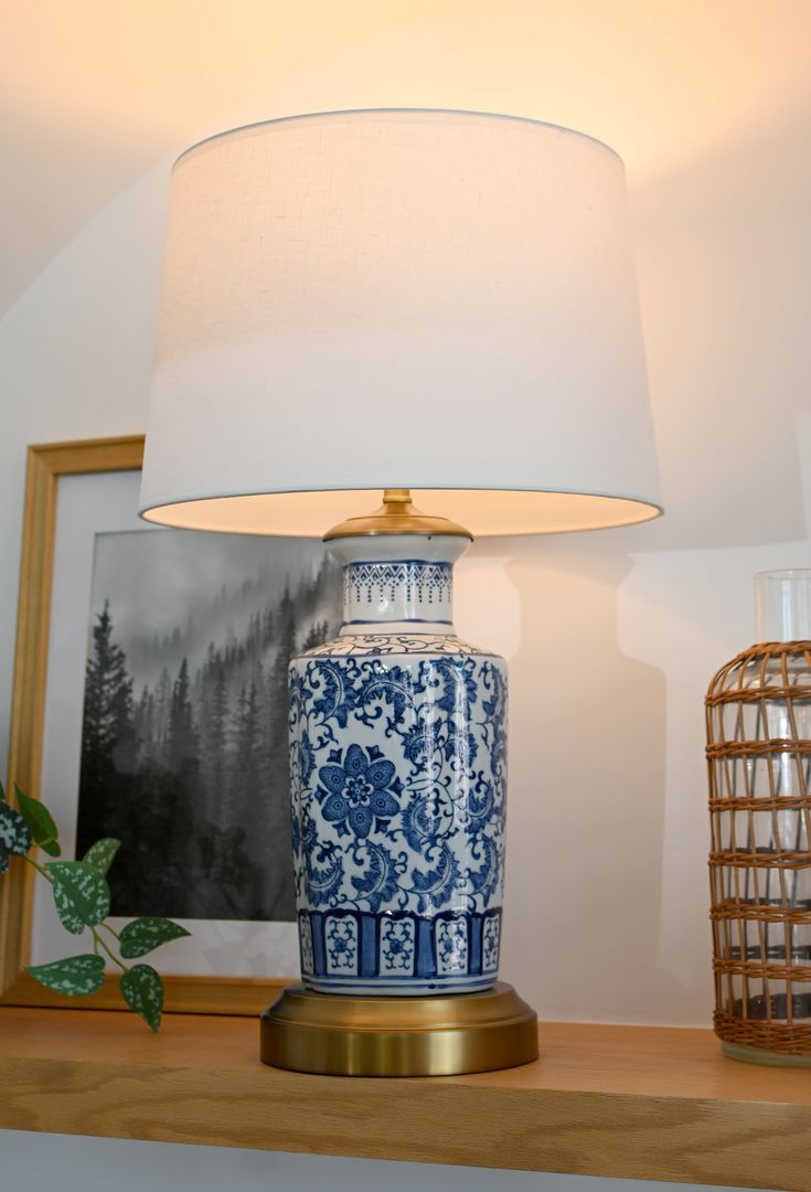 a blue and white vase sitting on top of a wooden shelf next to a lamp