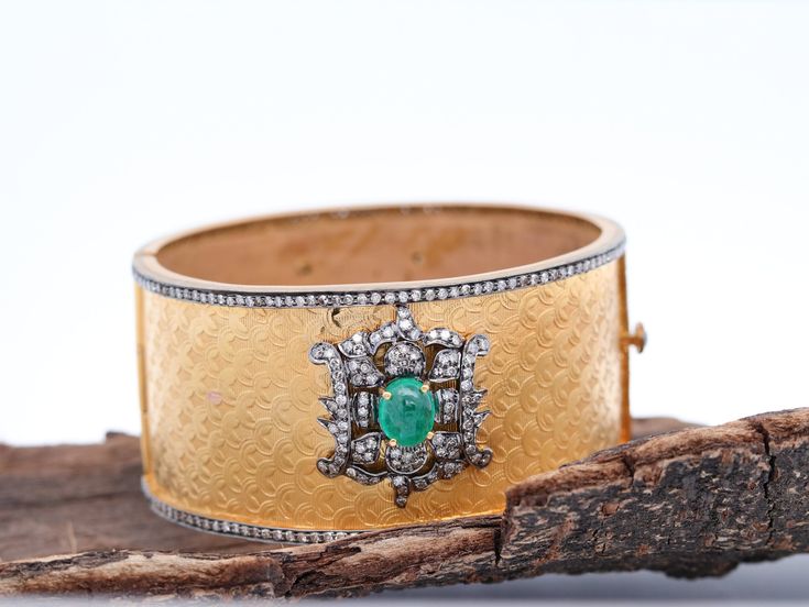 Discover Uniqueness in Every Detail with our Two-Tone Diamond and Emerald Bangle One of a Kind Design: This exquisite bangle is a true work of art, featuring a stunning textured design. It's expertly set in a combination of 14kt Yellow Gold and Sterling Silver, adorned with Pave Diamonds and lustrous Emeralds. The intricate scallop texturing and the motif design housing Diamonds and Emeralds make this bangle a truly unique piece of jewelry. The cuff opens from the side, and the closure is adorned with Diamond Polki, adding to its allure. The two-tone effect of the metals ensures this bangle stands out in any crowd. Details: - Gross Weight: 57.72 gms - 14k Gold Weight: 48.00 gms - Silver Weight: 7.23 gms - Diamond Weight: 4.10 cts - Emerald Weight: 8.60 cts - Dimensions:   - Inner Diameter: Luxury Jeweled Bangle, Luxury Jeweled Bangle For Formal Occasions, Fine Jewelry Diamond Accents Bangle For Wedding, Fine Jewelry Wedding Bangle With Diamond Accents, Luxury Jeweled Bangle Bracelets, Wedding Fine Jewelry Bangle With Diamond Accents, Wedding Bangle With Diamond Accents, Fine Jewelry Wedding Bangle With 17 Jewels, Luxury Jeweled Bangle Cuff Bracelet