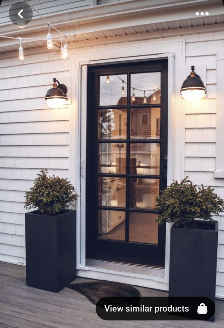 two black planters sitting on the side of a house with lights hanging above them