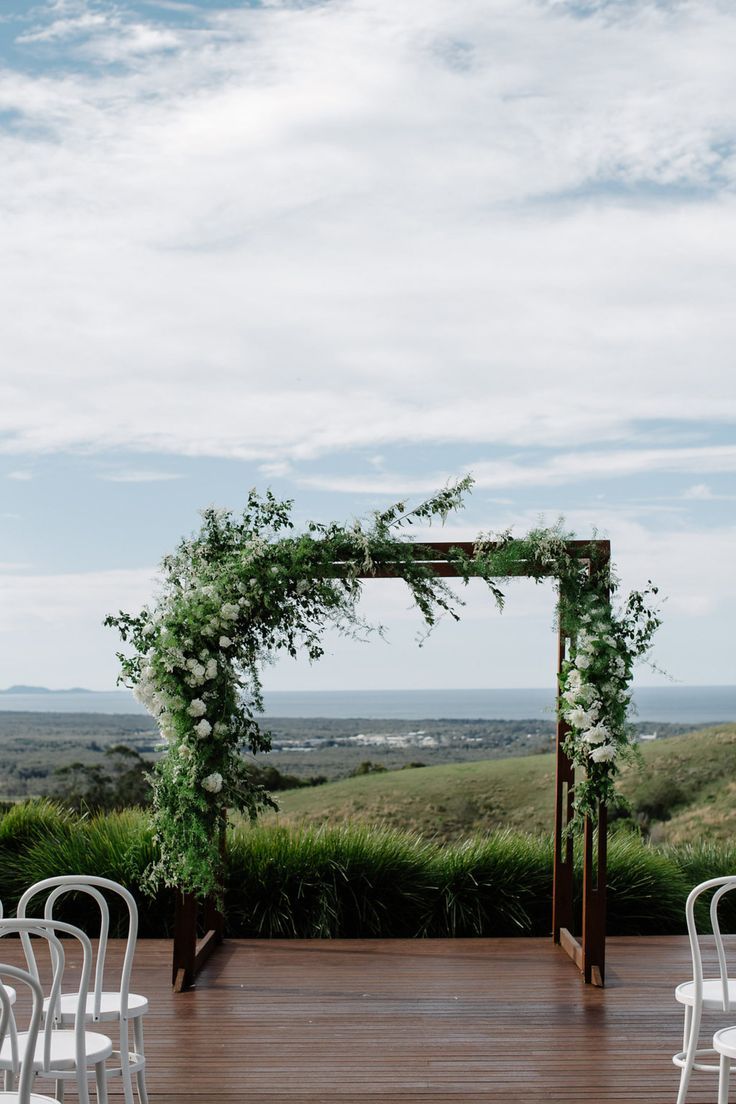 an outdoor ceremony setup with white chairs and greenery on the ground, in front of a scenic view