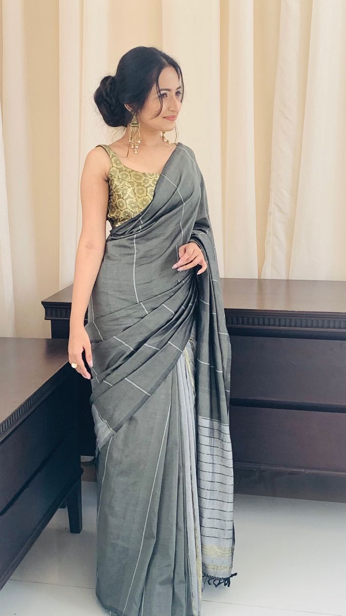 a woman standing in front of a desk wearing a gray sari