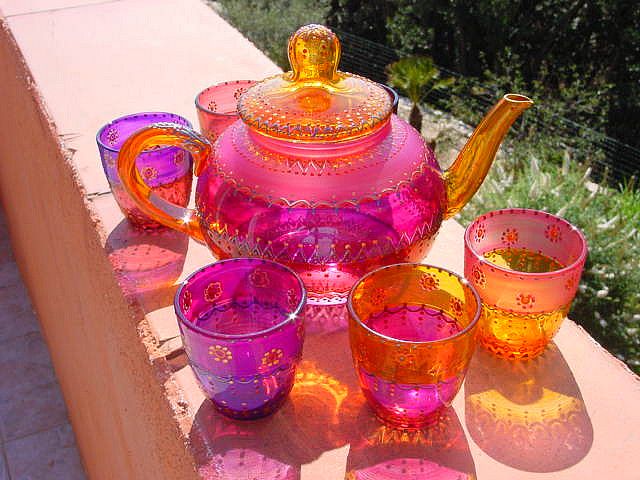 a pink tea set with cups and saucers on a table outside in the sun