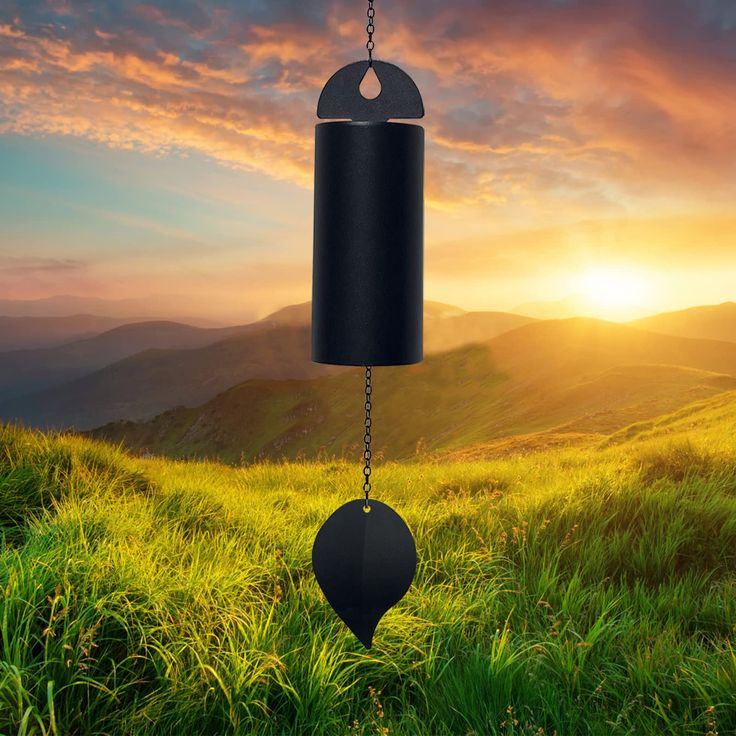 a wind chime hanging from a chain in the middle of a grassy field at sunset