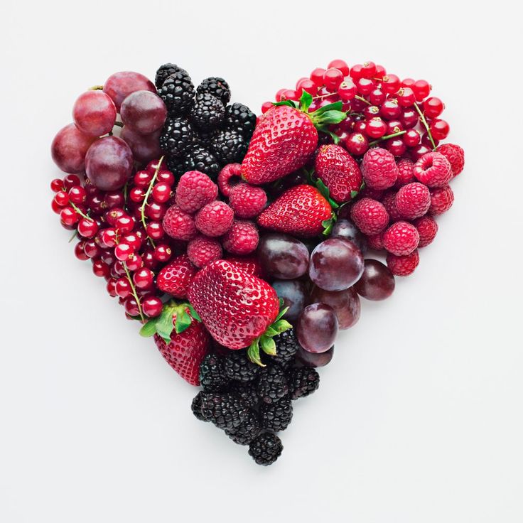 a heart shaped arrangement of berries, grapes and raspberries on a white background