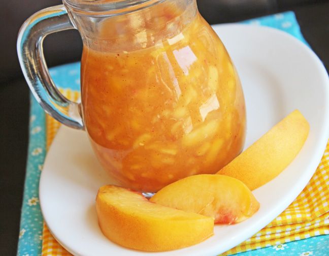 a glass jar filled with liquid sitting on top of a plate next to sliced peaches