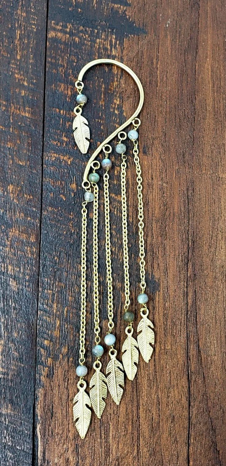 a gold chain with leaves and beads hanging from it on a wooden table next to a pair of scissors