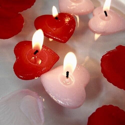 several candles with red hearts on them sitting in a bowl filled with water and rose petals