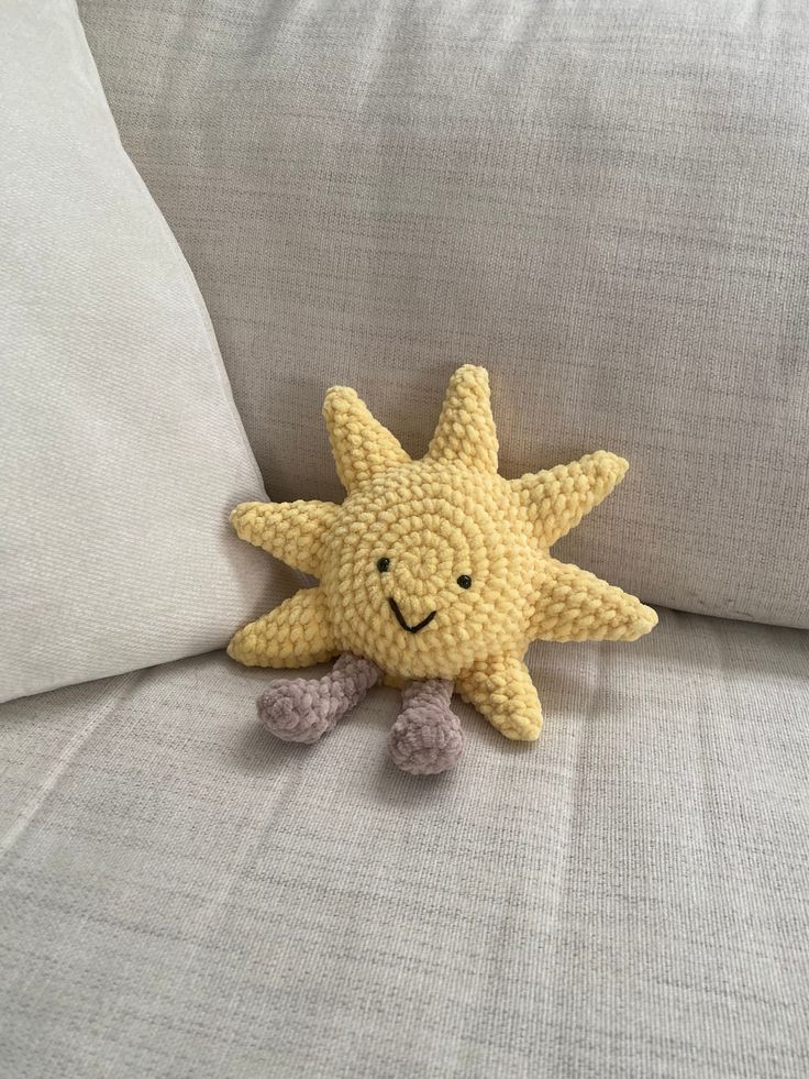 a crocheted yellow starfish sitting on top of a white couch cushion with two pillows