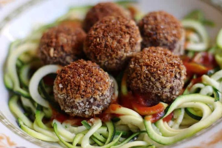 some meatballs are sitting on top of zucchini noodles in a white bowl