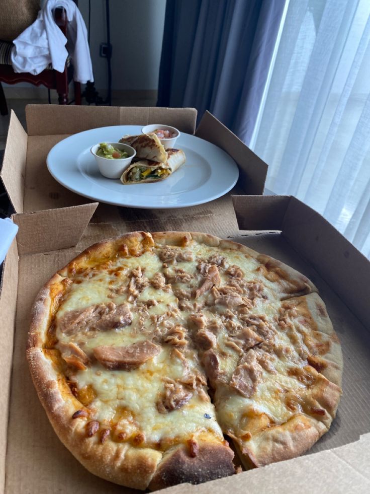 a pizza sitting on top of a cardboard box next to a plate with food in it