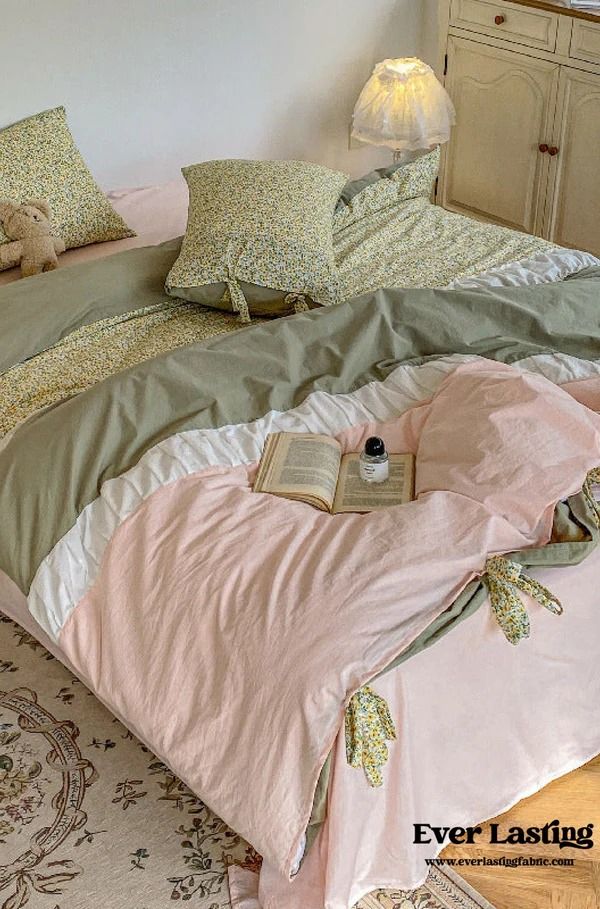 a bed with pink and green comforter next to a night stand in a bedroom