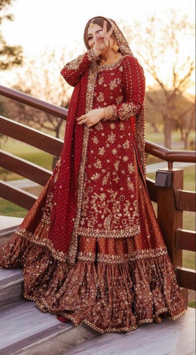 a woman in a red and gold bridal gown standing on a wooden deck with her hands to her face