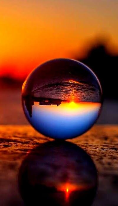 the sun is setting behind a glass ball with reflection on it's surface in front of an orange and blue sky