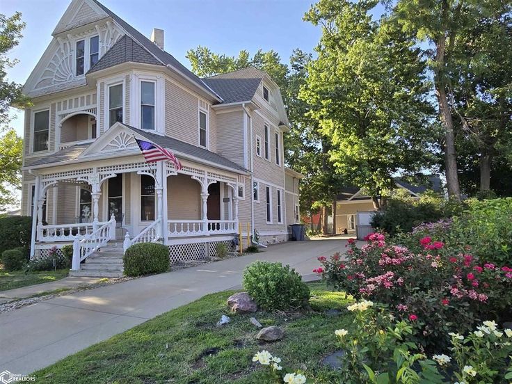 a large house with an american flag on the porch and flowers in front of it