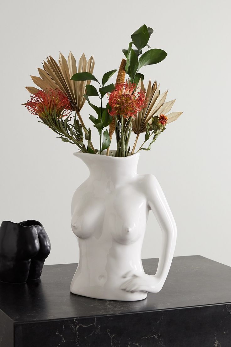 a vase with flowers in it sitting on a table next to a black object that looks like a human torso