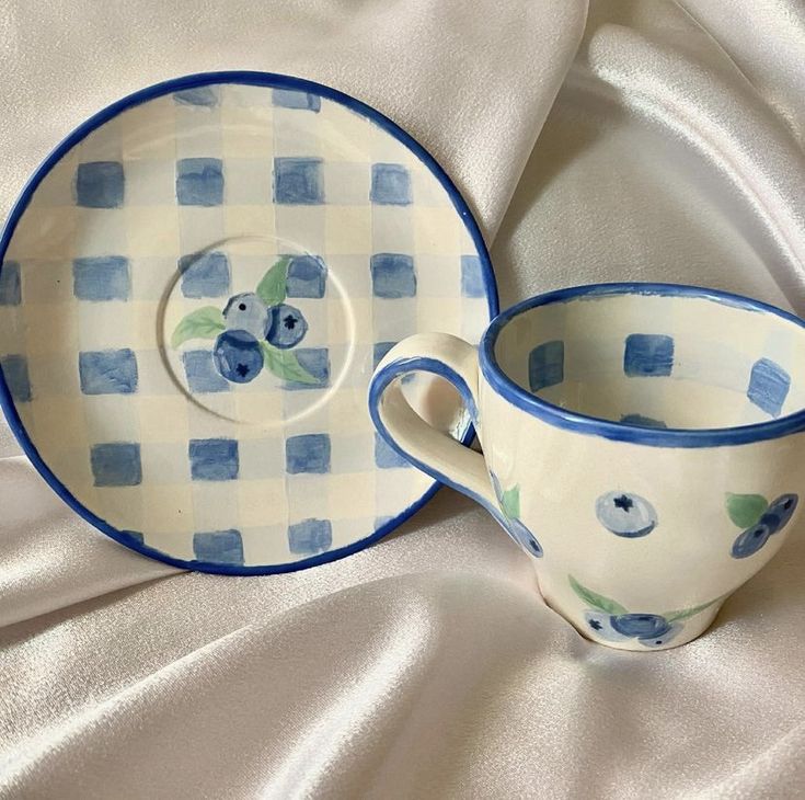 two cups and saucers are sitting on a white tablecloth with blue checkered designs