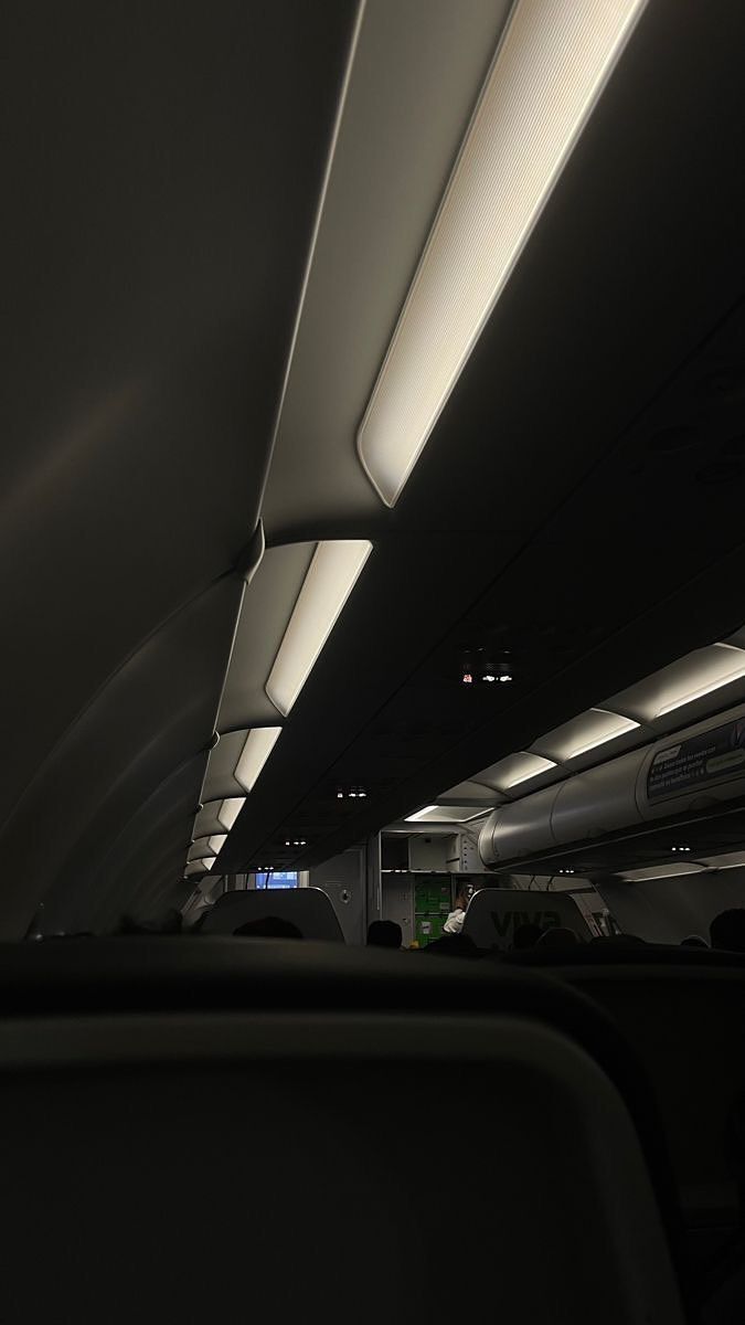 the interior of an airplane with lights on and overhead lighting in the back ground area