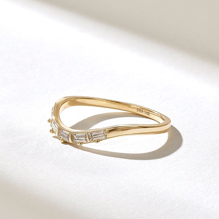 a yellow gold ring with three baguettes on the side, sitting on a white surface