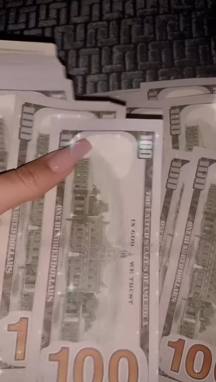 a hand is pointing at several stacks of hundred dollar bills in front of a computer keyboard