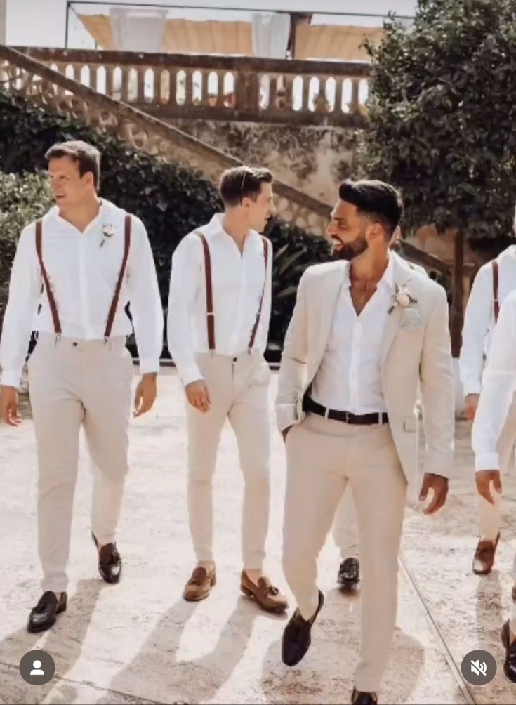 a group of men standing next to each other wearing white suits and brown suspenders