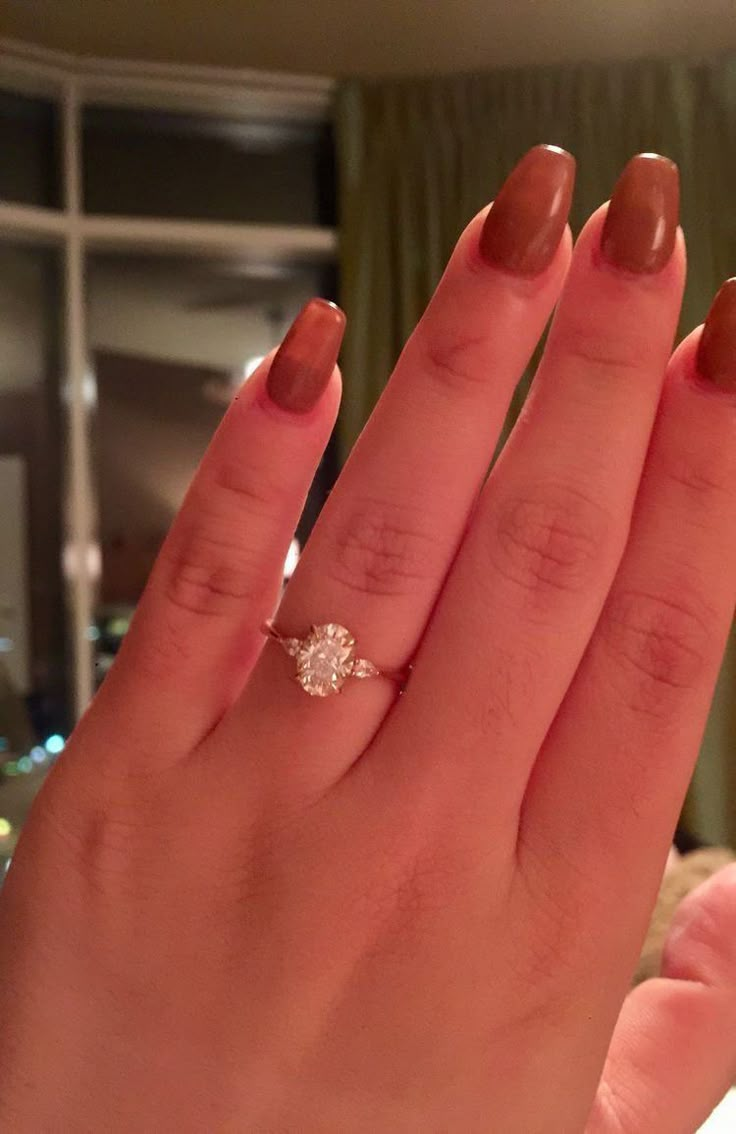 a woman's hand with a diamond ring on her left hand, in front of a window