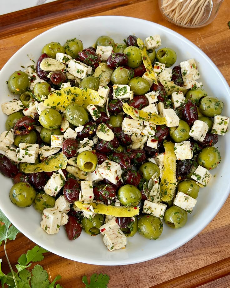 a white bowl filled with olives and feta cheese on top of a wooden table