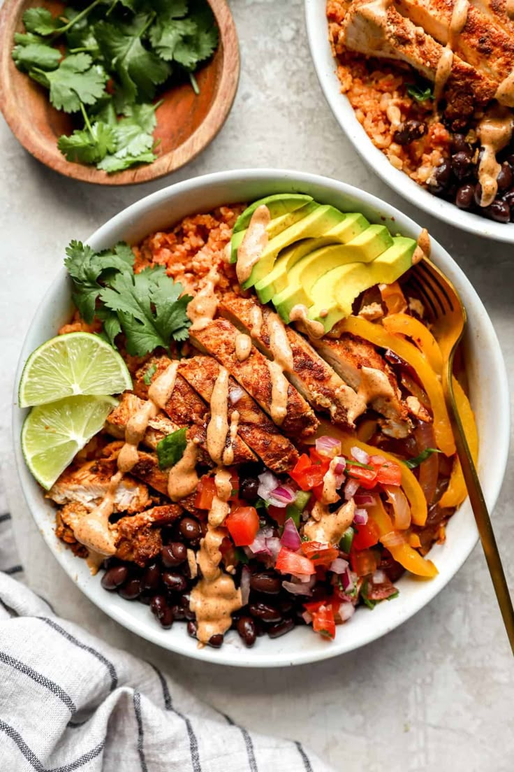 two bowls filled with chicken, black beans and avocado on top of a table