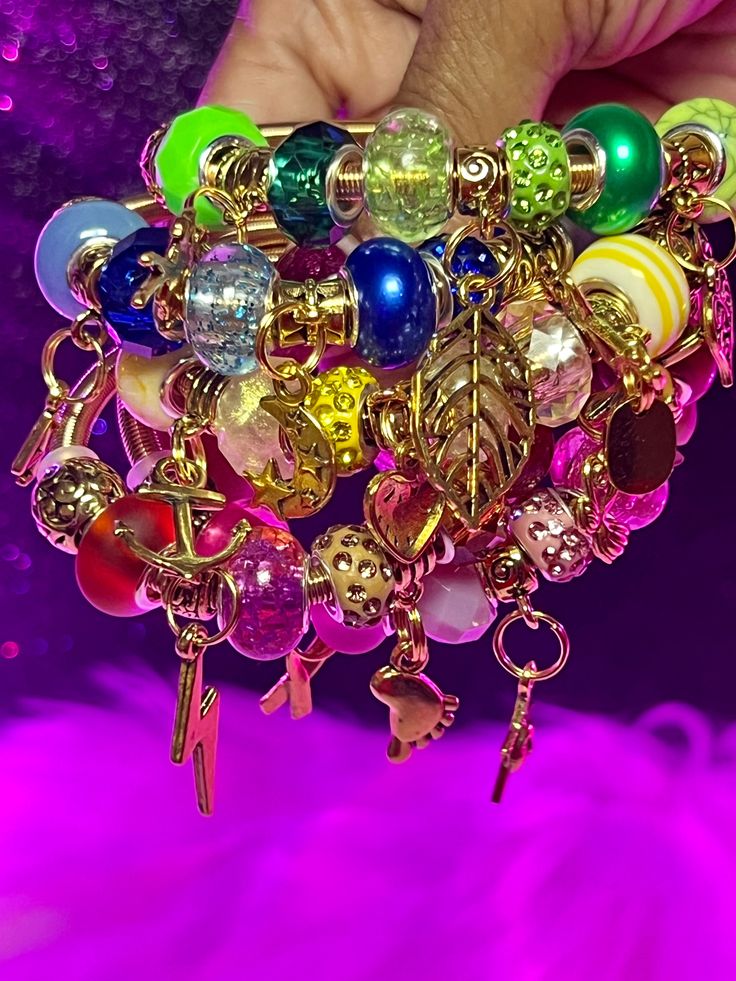 a person is holding a bunch of colorful beads and charms in their hand, while the background is blurry