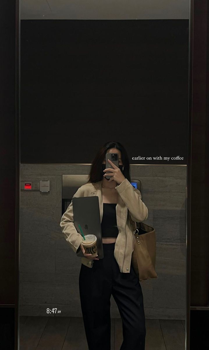 a woman taking a selfie in an elevator while holding a laptop and coffee cup