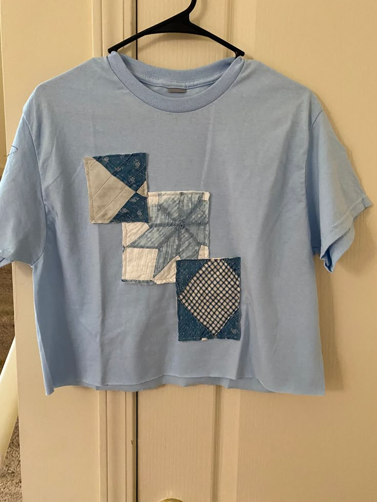 a blue t - shirt with patchwork on it hanging from a door