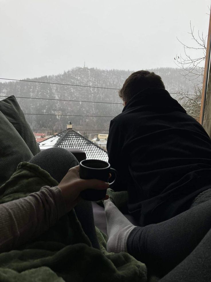 a person sitting on a couch with a cup in their hand and looking out the window